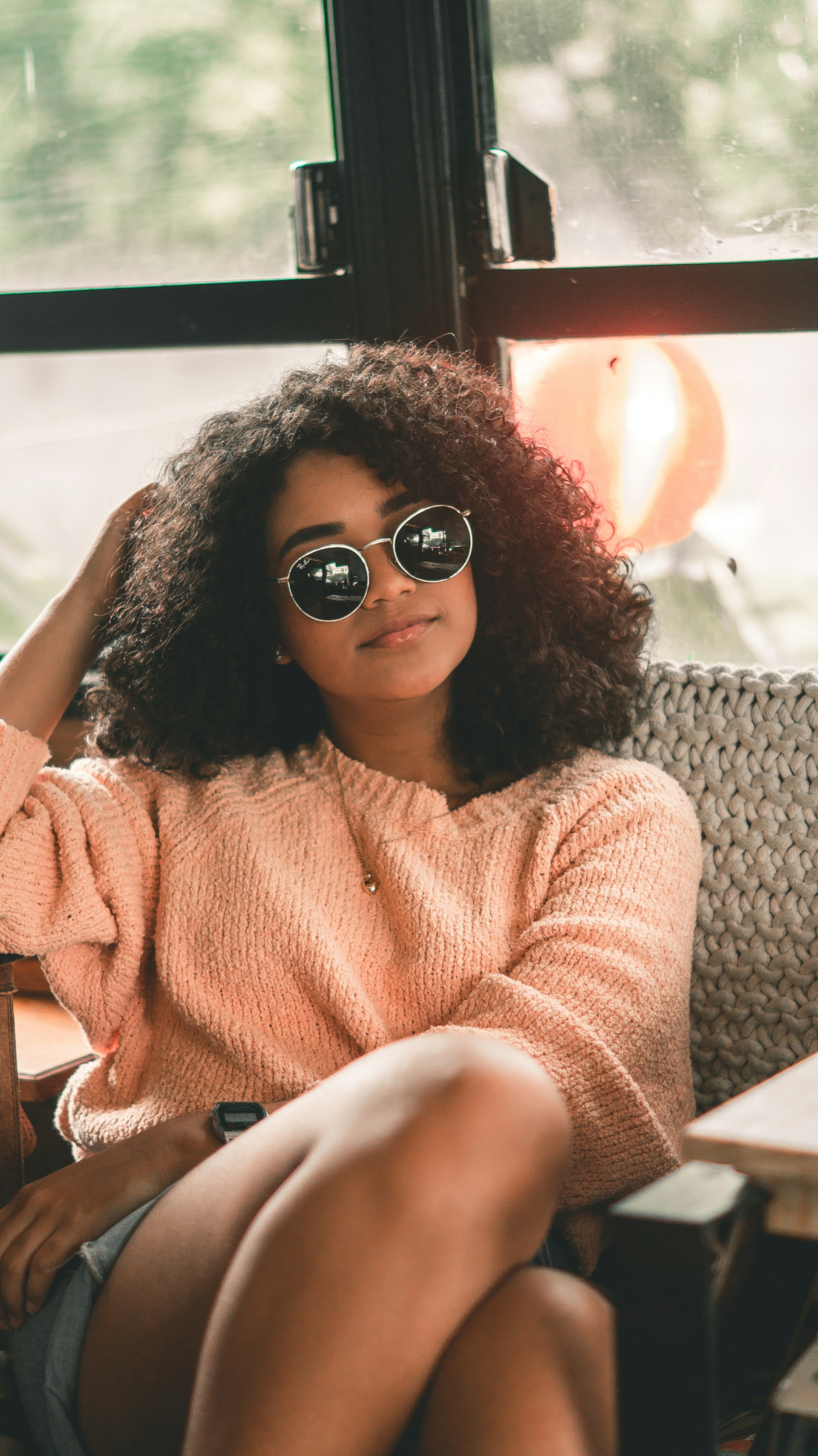 Foto von Mila. Sie hat dunkle Haare und trägt eine Sonnenbrille und einen Pullover.