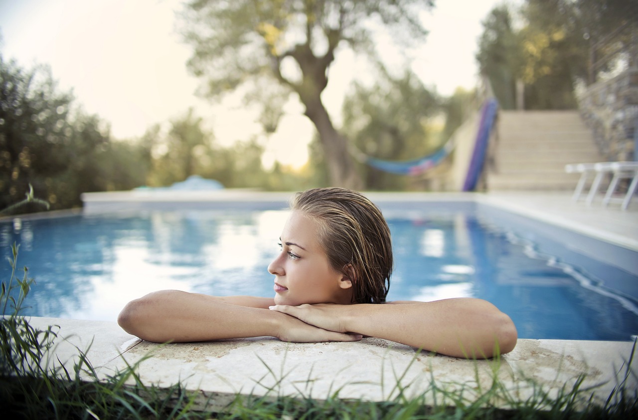 Foto einer Frau, die in einem Pool mit dem Kopf gestützt am Rand steht.