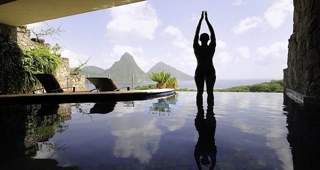 Foto einer Frau im Wasser eines Pools stehend, daneben Liegen und im Hintergrund schöne Landschaft.